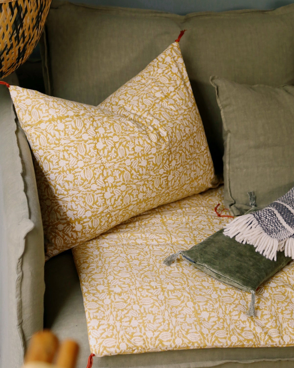 Housse de coussin Tulipan à motifs Curcuma sur un canapé vert