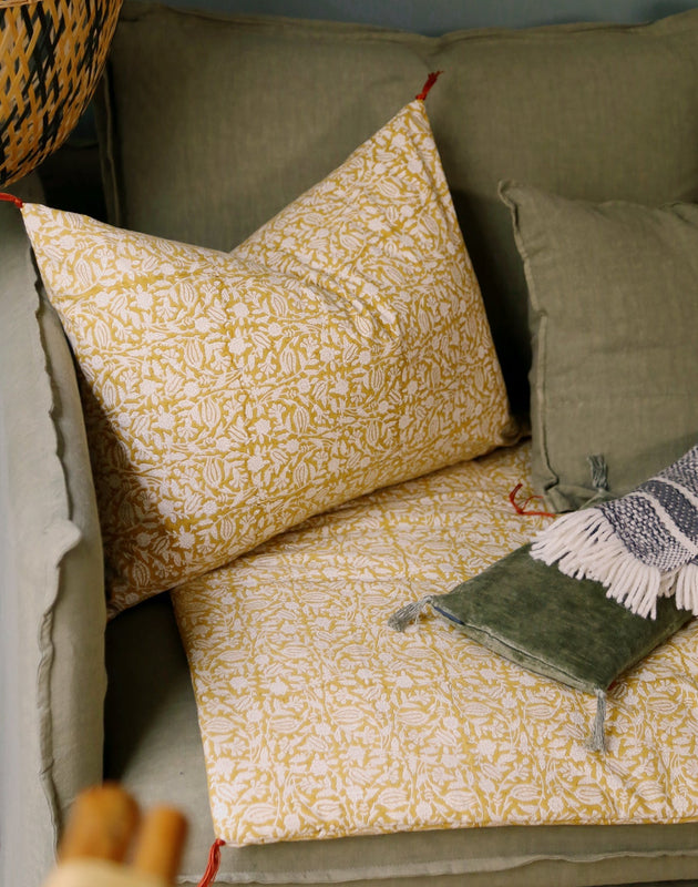 Housse de coussin Tulipan à motifs Curcuma sur un canapé vert