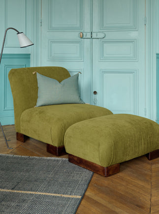 La chauffeuse Pacha et son repose-pieds à la structure en hêtre massif et au tissu en lin Gareth dans un salon élégant. 