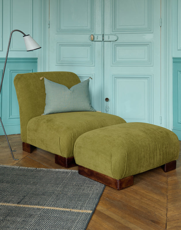 La chauffeuse Pacha et son repose-pieds à la structure en hêtre massif et au tissu en lin Gareth dans un salon élégant. 