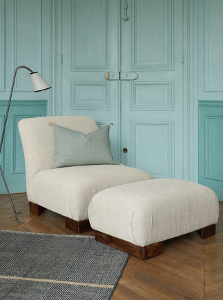 La chauffeuse Pacha et son repose-pieds à la structure en hêtre massif et au tissu en lin Gareth dans un salon élégant. 