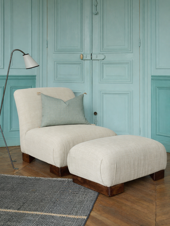 La chauffeuse Pacha et son repose-pieds à la structure en hêtre massif et au tissu en lin Gareth dans un salon élégant. 