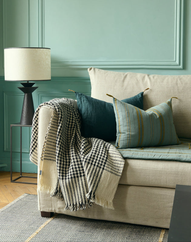 Salon bleu avec un canapé et ses coussins Noely en coton et Luni accompagné de la lampe Rosha en bout de canapé.